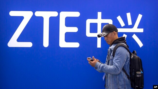 FILE - A man looks at his smartphone as he stands near a display for Chinese technology company ZTE at the PT Expo in Beijing on Oct. 31, 2019.