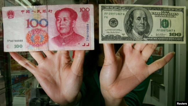 香港一家货币兑换店里的雇员展示人民币和美元百元钞票（2016年5月16日）。