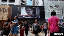 People cross a street in front of a monitor showing file footage of Edward Snowden, a former contractor for the U.S. National Security Agency (NSA), with a news tag (L) saying he has left Hong Kong, in Hong Kong June 23, 2013. 