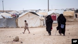 FILE - Women walk in the al-Hol camp that houses some 60,000 refugees, including families and supporters of the Islamic State group, many of them foreign nationals, in Hasakeh province, Syria, May 1, 2021. France said Tuesday it repatriated 25 children and 10 women from a camp.