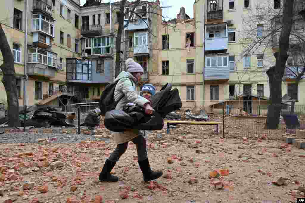 A local resident carries her baby outside of their residential building partially destroyed after a missile strike in Kharkiv, Ukraine. (Photo by SERGEY BOBOK / AFP)