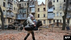 A local resident carries her baby outside of their residential building partially destroyed after a missile strike in Kharkiv, Ukraine, Jan. 30, 2023