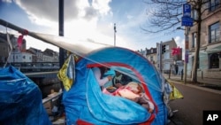FILE - Two men share a meal in a makeshift tent camp outside the Petit Chateau reception center in Brussels, Jan. 17, 2023