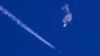 FILE - In this photo provided by Chad Fish, the remnants of a large balloon drift above the Atlantic Ocean, just off the coast of South Carolina, with a fighter jet and its contrail seen below it, Feb. 4, 2023.