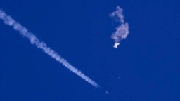 FILE - In this photo provided by Chad Fish, the remnants of a large balloon drift above the Atlantic Ocean, just off the coast of South Carolina, with a fighter jet and its contrail seen below it, Feb. 4, 2023.