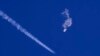 In this photo provided by Chad Fish, the remnants of a large balloon drift above the Atlantic Ocean, just off the coast of South Carolina, with a fighter jet and its contrail seen below it, Feb. 4, 2023.