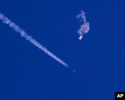 In this photo provided by Chad Fish, the remnants of a large balloon drift above the Atlantic Ocean, just off the coast of South Carolina, with a fighter jet and its contrail seen below it, Feb. 4, 2023.