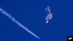 FILE - In this photo provided by Chad Fish, the remnants of a large balloon drift above the Atlantic Ocean, just off the coast of South Carolina, with a fighter jet and its contrail seen below it, Feb. 4, 2023.