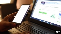 လက်တော့ကွန်ပြူတာတလုံးရှေ့တွင် အမျိုးသမီးတဦး မိုဘိုင်းဖုန်းအသုံးပြုနေပုံ