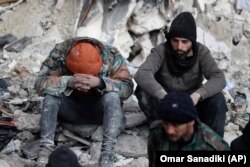 People react as they sit on the wreckage of collapsed buildings, in Aleppo, Syria, Tuesday, Feb. 7, 2023. (AP Photo/Omar Sanadiki)