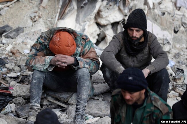 People react as they sit on the wreckage of collapsed buildings, in Aleppo, Syria, Tuesday, Feb. 7, 2023. (AP Photo/Omar Sanadiki)