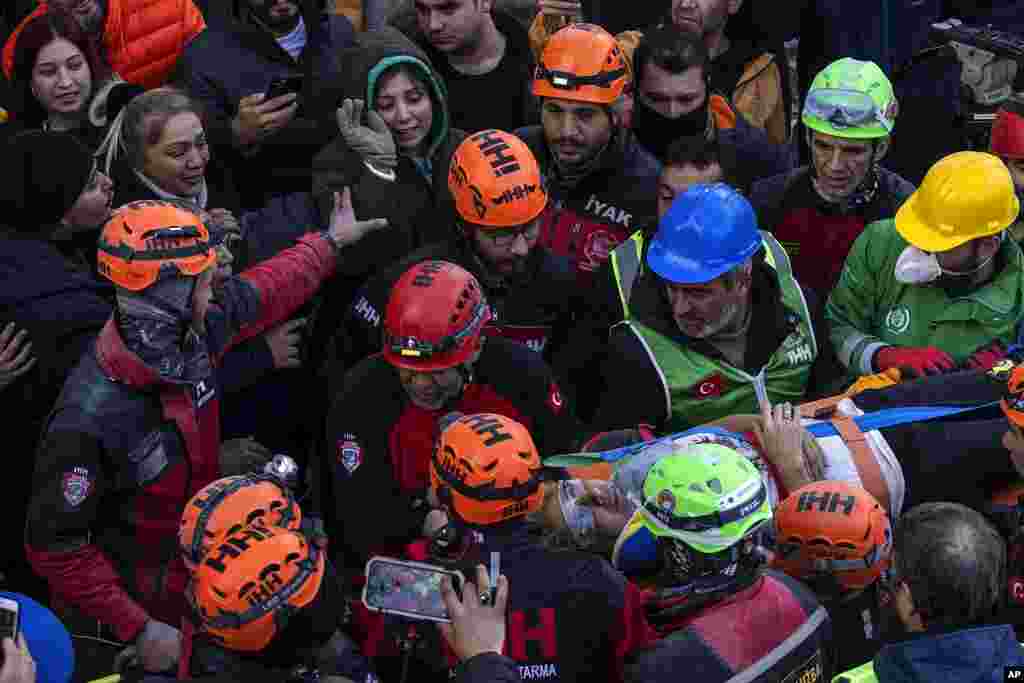 Raziye Kilinc is carried through a crowd on a stretcher after she was rescued under a destroyed building as her daughter, center, with the green black hood, waves in Iskenderun, southeastern Turkey.