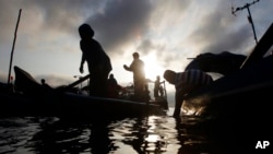 FILE - Fishermen are silhouetted as they arrive their wooden boats at the river bank after they collect fish on the Mekong River during the fish-harvesting season near Phnom Penh, Cambodia, Nov. 28, 2018. 