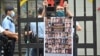 FILE - A protester stands behind mock jail bars with photos of imprisoned pro-democracy figures to be tried under the National Security Law, in Hong Kong, Sept. 19, 2021. 