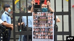 FILE - A protester stands behind mock jail bars with photos of imprisoned pro-democracy figures to be tried under the National Security Law, in Hong Kong, Sept. 19, 2021. 