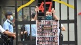 资料照片：2021年9月19日，香港一名抗议者站在模拟监狱铁窗后面，手里拿着根据《国家安全法》受审的民主派人士的照片。（法新社照片）