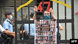 资料照片：2021年9月19日，香港一名抗议者站在模拟监狱铁窗后面，手里拿着根据《国家安全法》受审的民主派人士的照片。（法新社照片）