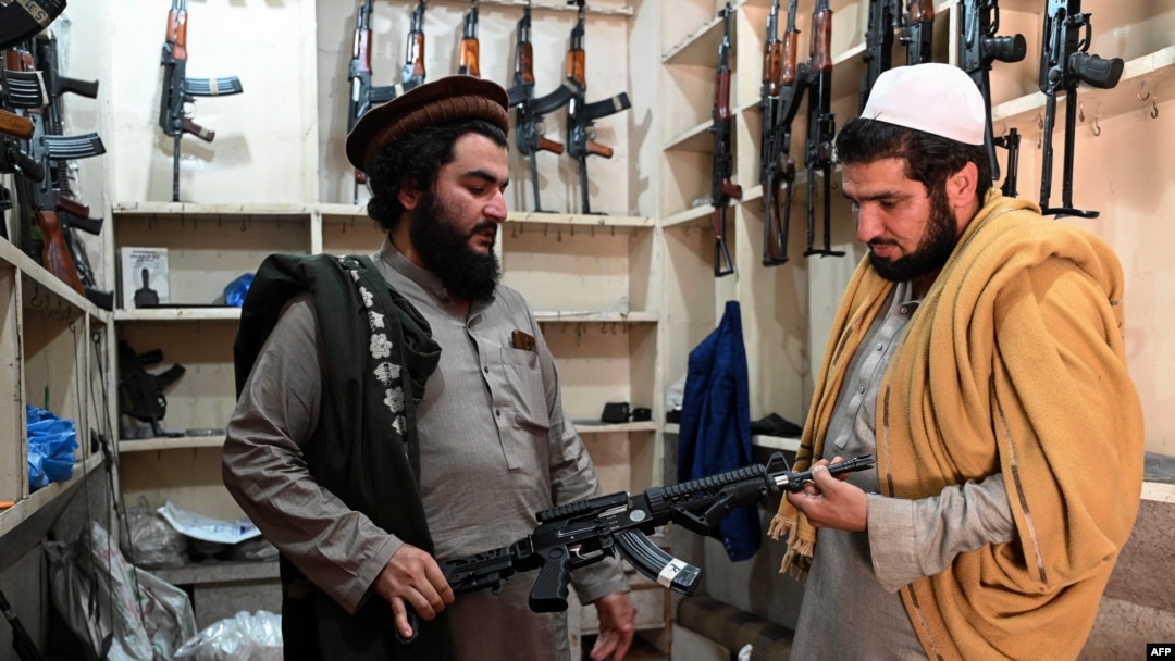 Arms dealer Hakimullah Afridi, left, displays a locally made automatic weapon to a customer at his shop in Darra Adamkhel, south of Peshawar, Pakistan, Dec. 14, 2022.