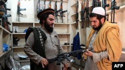 Arms dealer Hakimullah Afridi, left, displays a locally made automatic weapon to a customer at his shop in Darra Adamkhel, south of Peshawar, Pakistan, Dec. 14, 2022.