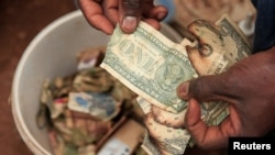 FILE - Cuthbert Gudza, 33, a street money trader, repairs damaged U.S. banknotes, outside a shopping centre, in Kuwadzana township, Harare, Zimbabwe, Jan. 18, 2023.