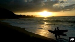 FILE - Participants in the Eddie Aikau surfing contest walk out of the ocean at sunset after the opening ceremony in Waimea Bay near Haleiwa, Hawaii, on Nov. 30, 2006.