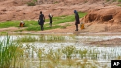 In this Wednesday Oct. 4, 2017 photo, children in the town of Terekeka draw water from a stagnant pond that was once infected with Guinea Worm when the town was endemic. (AP Photo/Mariah Quesada)