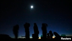 FILE - The moon shines above a group of people on the lookout for unidentified flying objects tour in the desert outside Sedona, Arizona, Feb. 14, 2013. 