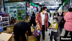 FILE - A woman and a child walk past workers sorting toys at a shopping mall in Beijing, Jan. 11, 2023. 