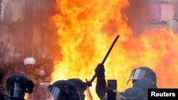 Flames from a fire rise behind law enforcement officers during a demonstration against the French government's pension reform plan as part of the fourth day of national protests, in Paris, France, Feb. 11, 2023.