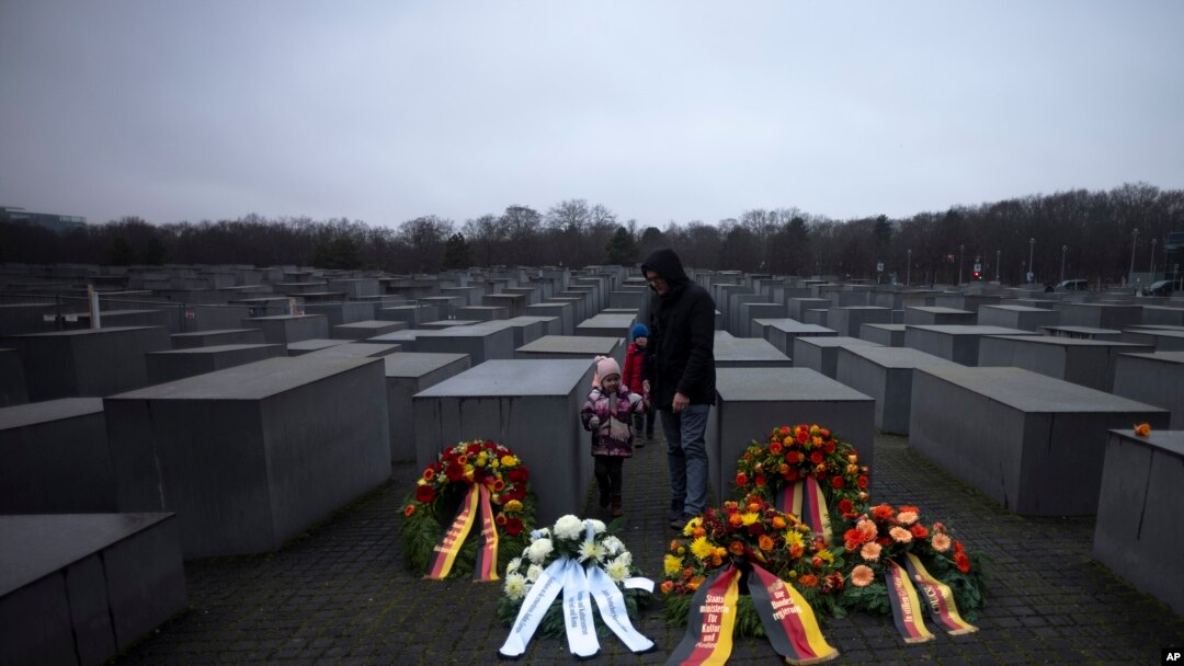 Seorang ayah dengan kedua anaknya berdiri di karangan bunga pada hari Peringatan Holokos Internasional di Berlin, Jerman, 27 Januari 2023.