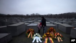 Seorang ayah dengan kedua anaknya berdiri di karangan bunga pada hari Peringatan Holokos Internasional di Berlin, Jerman, 27 Januari 2023.