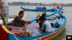 FILE - Cambodians collect fish from the fishing net on their family's wooden boat on Mekong River near Phnom Penh, Cambodia, May 29, 2019.