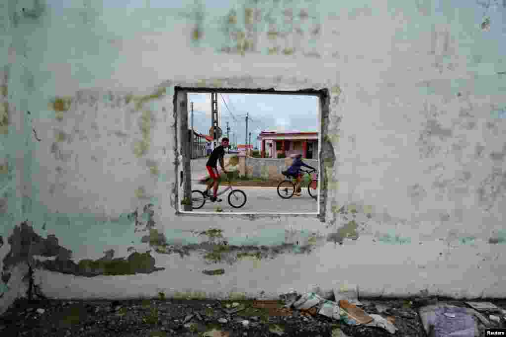 Деца возат велосипеди и поминуваат покрај напуштена зграда во Изабела де Сагуа, Куба.