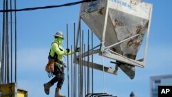 A worker guides a bin into position at a construction site, Jan. 24, 2023, in Miami.