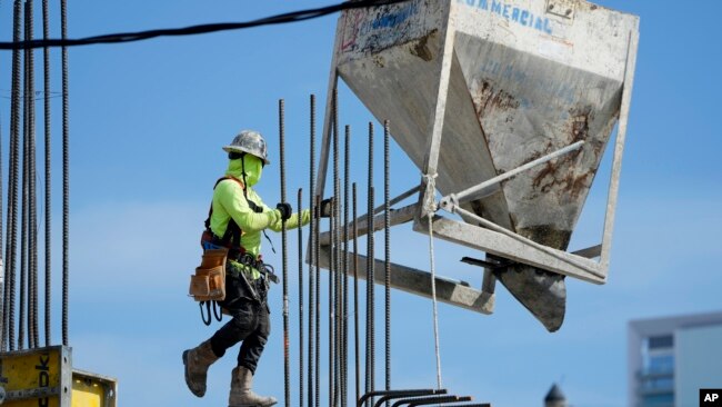 A worker guides a bin into position at a construction site, Jan. 24, 2023, in Miami.
