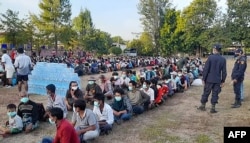 FILE - This photo taken Dec. 16, 2021 by Metta Charity shows people from Myanmar waiting to be processed in Thailand's Mae Sot district near the border, as Thai military personnel look on.