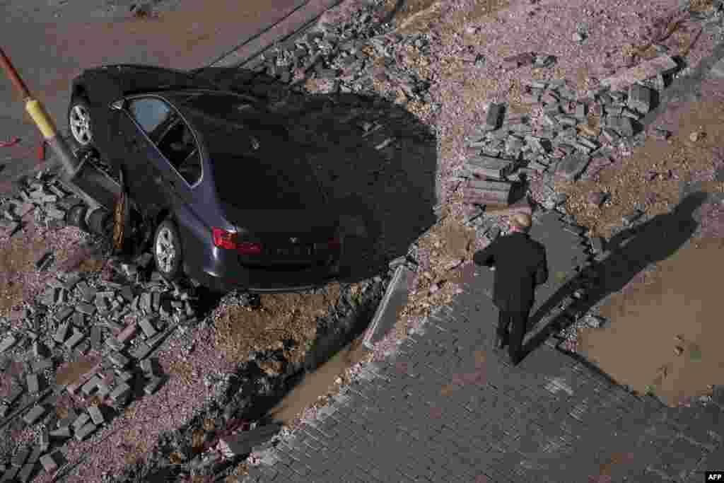 A pedestrian walks by a car on a damaged street after heavy rain in Kosovo.