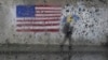 FILE - A pedestrian carries an umbrella while walking past a painting of an American flag in San Francisco, Jan. 11, 2023.