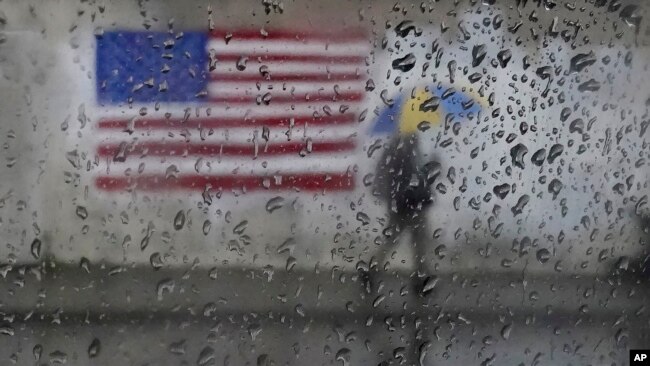 FILE - A pedestrian carries an umbrella while walking past a painting of an American flag in San Francisco, Jan. 11, 2023.