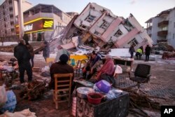 Beberapa penyintas gempa duduk dan berdiri di sekitar bangunan yang runtuh di kota Golbasi, provinsi Adiyaman, Turki selatan, 8 Februari 2023.