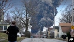 A man takes photos as a black plume rises over East Palestine, Ohio, as a result of a controlled detonation of a portion of the derailed Norfolk and Southern trains, Feb. 6, 2023.