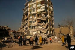 People stand by a collapsed building in Kahramanmaras, southern Turkey, Feb. 12, 2023.