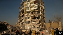 People stand by a collapsed building in Kahramanmaras, southern Turkey, Feb. 12, 2023. 