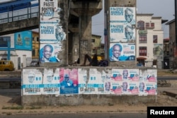 FILE - A man sleeps under a bridge decorated with electoral campaign posters, ahead of Nigeria's presidential elections, in Lagos, Nigeria, Jan. 31, 2023.