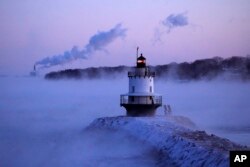 Spring Point Ledge Light is surrounded by arctic sea smoke while emissions from the Wyman Power plant, background, are blown horizontal by the fierce wind, Feb. 4, 2023, in South Portland, Maine. The morning temperature was about -10 degrees Fahrenheit.