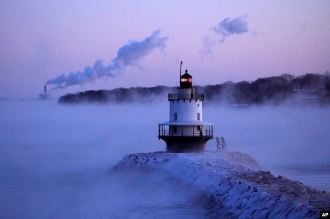 Spring Point Ledge Light is surrounded by arctic sea smoke while emissions from the Wyman Power plant, background, are blown horizontal by the fierce wind, Feb. 4, 2023, in South Portland, Maine. The morning temperature was about -10 degrees Fahrenheit.