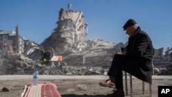 A man sits on a chair, as heavy machines remove debris from a building, where five of his family members are trapped in Nurdagi, southeastern Turkey, Feb. 9, 2023.