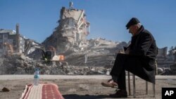 A man sits on a chair, as heavy machines remove debris from a building, where five of his family members are trapped in Nurdagi, southeastern Turkey, Feb. 9, 2023.