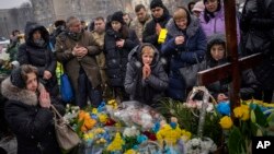 Nadia, center, prays at the grave of her son Oleg Kunynets, a Ukrainian military servicemen who were killed in the east of the country, during his funeral in Lviv, Feb 7, 2023.