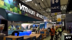 FILE - Some people walk past the VMware company stand as facilities for the Mobile World Congress in Barcelona, Spain, are set up on Feb. 20, 2016.